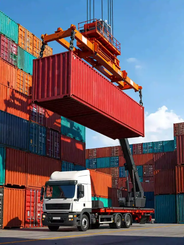 Grue portuaire soulevant un conteneur rouge au-dessus d'un camion blanc dans une zone de stockage logistique.