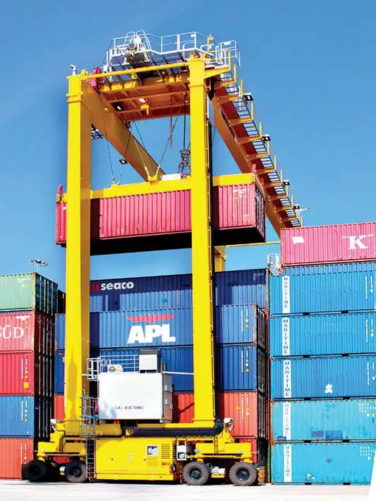 Un portique de manutention jaune déplaçant un conteneur maritime rouge au-dessus d'une pile de conteneurs de couleurs.
